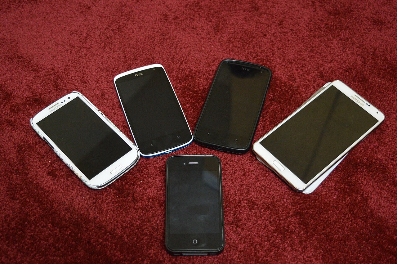 Five smartphones from different years on a red carpet