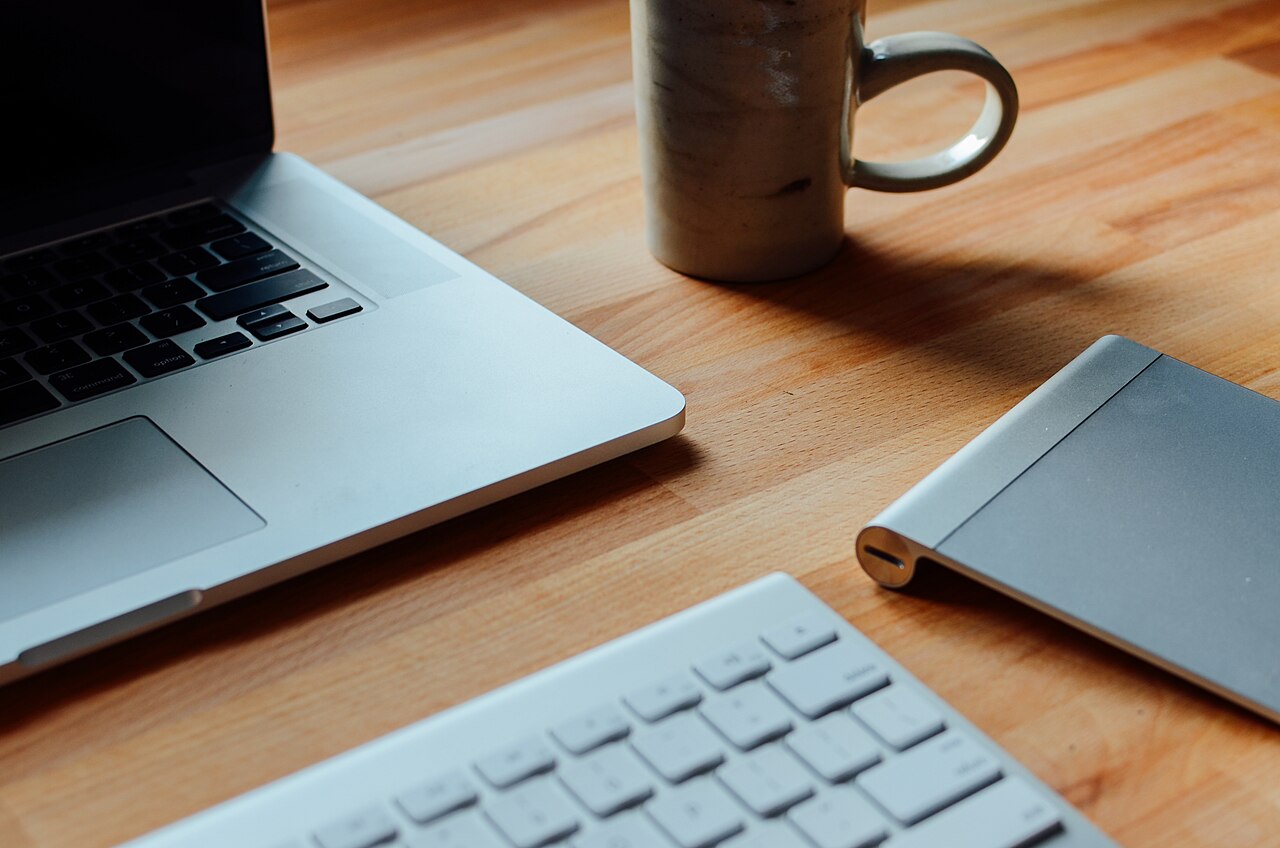 A laptop, keyboard and mug on a wooden desk
